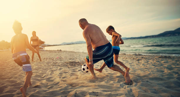 ビーチで祖父とサッカーをしている子供たち - beach football ストックフォトと画像