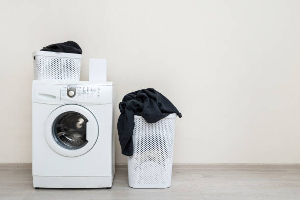 istock Preparation to laundry process. White washing machine with box of detergent soap and black clothes in basket standing on floor inside bright light flat interior 1137137436