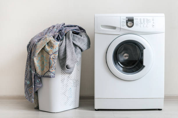 istock Preparation to laundry process. White washing machine and basket of clothes standing against wall inside flat with bright interior 1137137438