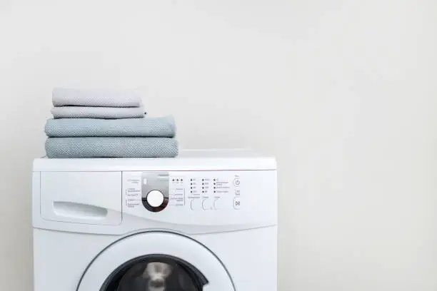 Photo of Laundry concept. Cropped photo of white and modern washing machine with fresh towel on top standing isolated inside bright apartment light interior