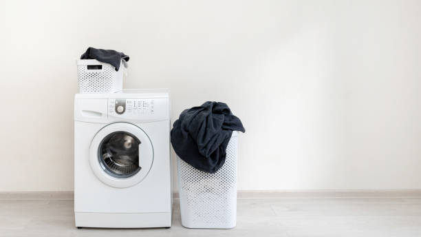 istock Photo of new white washing machine standing isolated inside flat with light interior with small and big laundry basket and copy space for text 1137138101