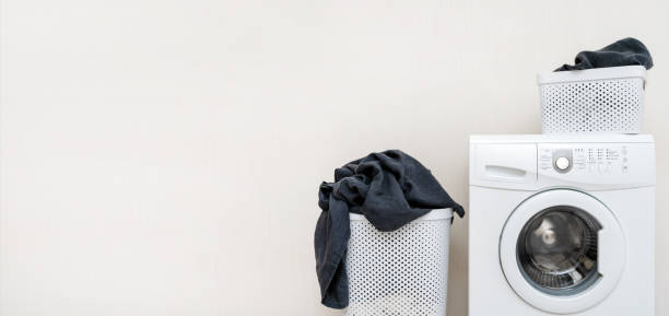 istock Laundry concept idea. White washing machine with two basket of black linen standing isolated inside apartment with light interior and copy space for text 1137138250