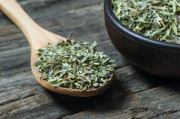 Photo of Heap of dry thyme in wooden spoon and in bowl on wooden background. Dried spice zahter thyme and oil concept