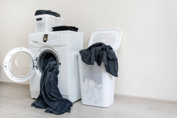istock Side view photo of modern washing machine and two laundry basket with textile standing inside bright light flat interior 1137140011