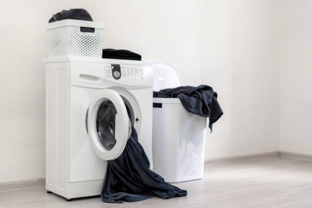 istock Laundry process concept. Low angle top view of new washing machine standing near white plastic basket inside light flat interior 1137140159