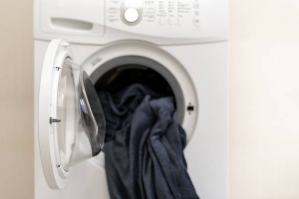 Laundry process concept. White washing machine with open door and blanket inside standing on flat with bright interior