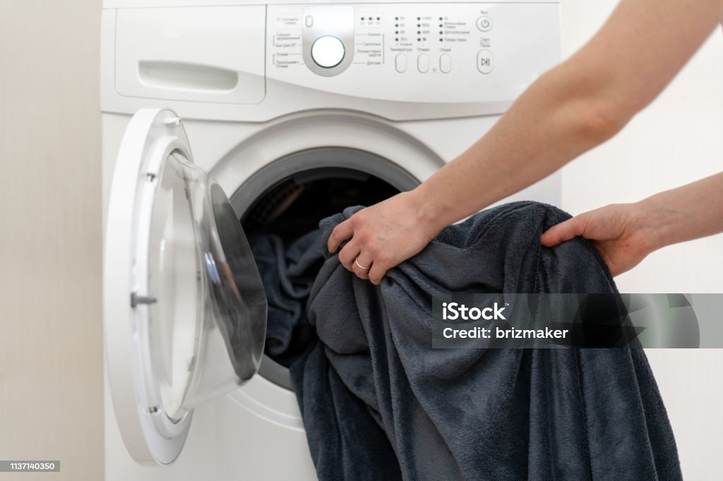 Cropped photo of woman hands put laundry into the white washing machine. She standing inside bright apartment with light interior Blanket Stock Photo