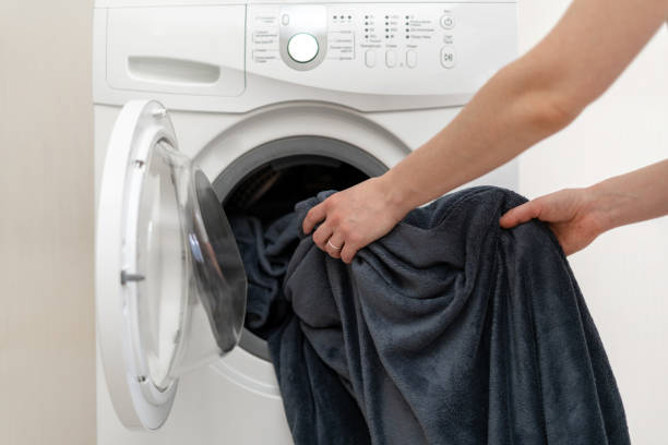 Cropped photo of woman hands put laundry into the white washing machine. She standing inside bright apartment with light interior Cropped photo of woman hands put laundry into the white washing machine. She standing inside bright apartment with light interior blanket stock pictures, royalty-free photos & images