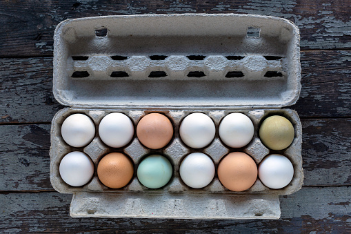 One dozen mixed color organic farm fresh white, brown, and blue eggs in a paper egg carton on a rustic wood background.