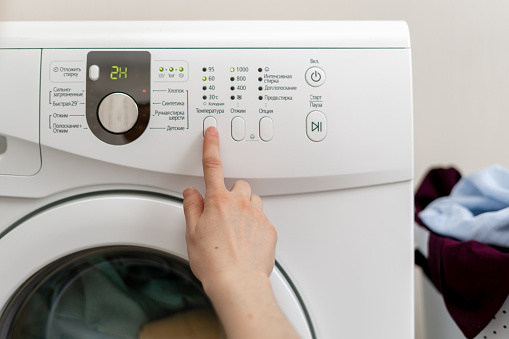 Cropped photo of choosing of laundry program. Woman select temperature on panel of washing machine inside bright apartment light interior