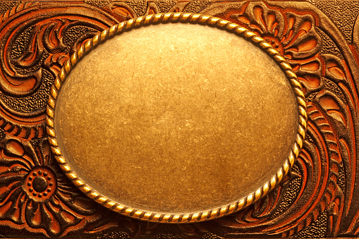 A gold oval shaped belt buckle resting on top of a tooled leather surface.