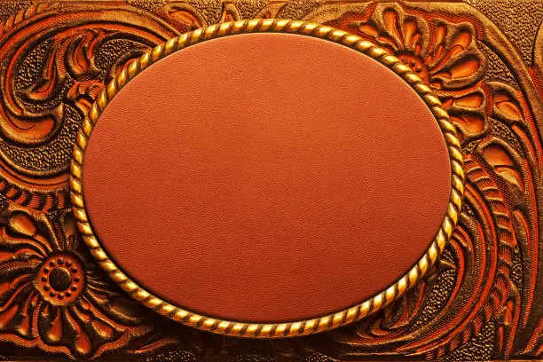 An oval shaped belt buckle resting on top of a tooled leather surface.