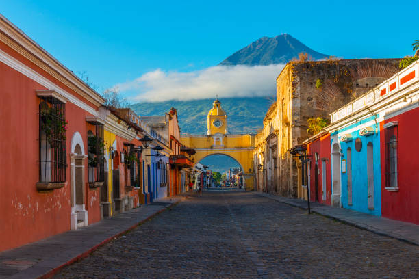 Cityscape of Antigua City, Guatemala Cityscape of the main street and yellow Santa Catalina arch in the historic city center of Antigua at sunrise with the Agua volcano, Guatemala. bell tower tower photos stock pictures, royalty-free photos & images