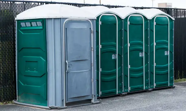 Green and gray potties set up in a parking lot with the end one for handicapped.