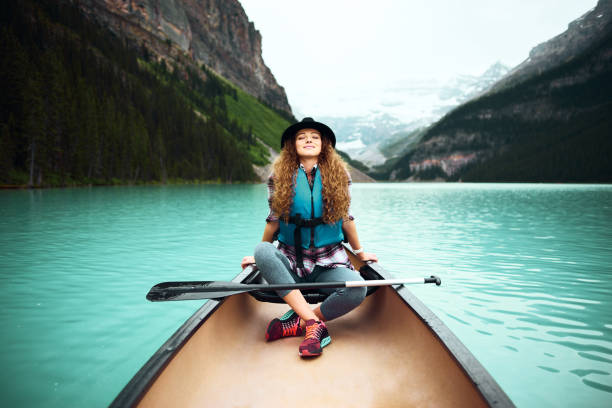 Smiling mature woman rowing boat in lake. Happy female is enjoying boating in forest. She is wearing casuals.
