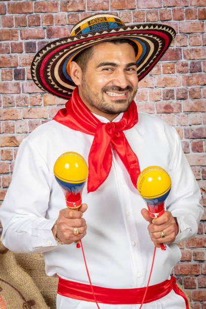 Colombian man playing maracas wearing typical coastal outfit Smiling mid adult Colombian man playing maracas wearing typical valledupar coastal outfit on a brick wall background traditional clothing stock pictures, royalty-free photos & images