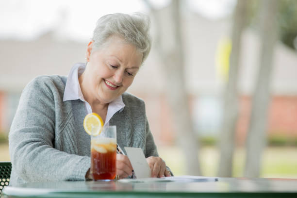 mujer mayor escribiendo tarjeta de felicitación para los nietos mientras está sentado en el porche trasero - texas tea fotografías e imágenes de stock