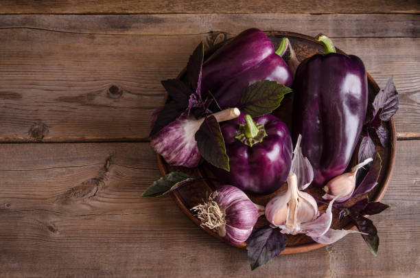 Dark purple peppers with leaves of basil and garlic on old rustic wooden table on black background stock photo