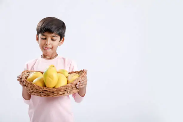 Photo of Cute indian/Asian little boy holding Mango basket in hand and giving multiple expressions. isolated over white background
