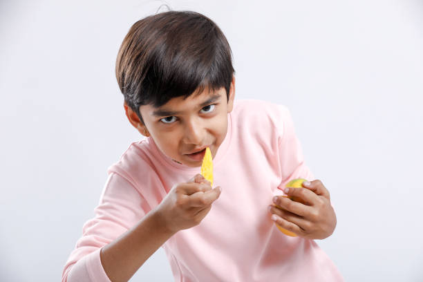 Cute indian/Asian little boy eating Mango with multiple expressions. isolated over white background