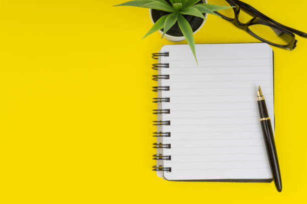 istock Workspace with black pen, spectacles, decoration flower and book on yellow background 1137271183