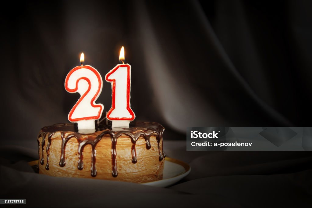 Twenty one years anniversary. Birthday chocolate cake with white burning candles in the form of number Twenty one. Dark background with black cloth Candle Stock Photo