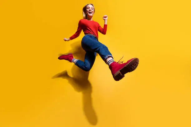 Photo of Low below angle full length body size view of nice attractive cheerful girl making step wearing vintage retro maroon burgundy footwear isolated over bright vivid shine orange background