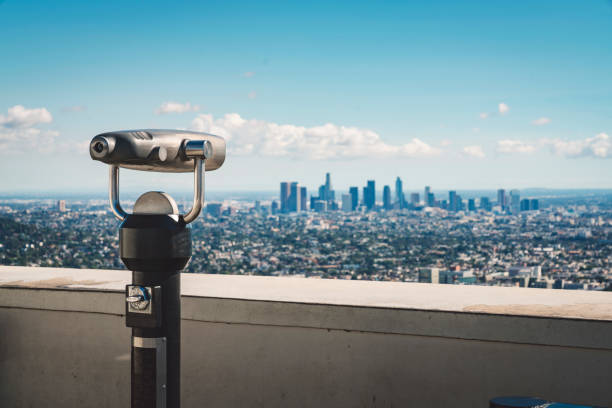 Young men looking on LA down town from Griffith observatory trough the telescope.