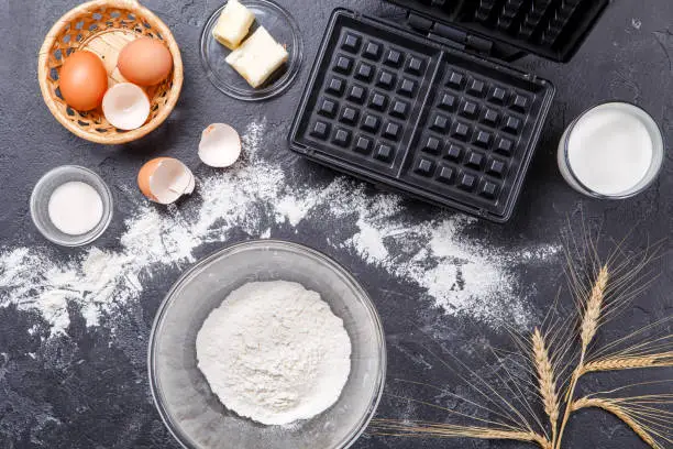 Photos on top of ingredients for Viennese waffles, waffle iron, spikelets on black, empty table