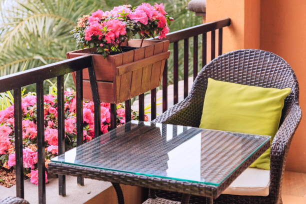 ratten mesa y sillón con almohadas en el balcón, con flores en macetas de azalea rosada en la barandilla con fondo verde palmeras. - leaf rhododendron summer spring fotografías e imágenes de stock