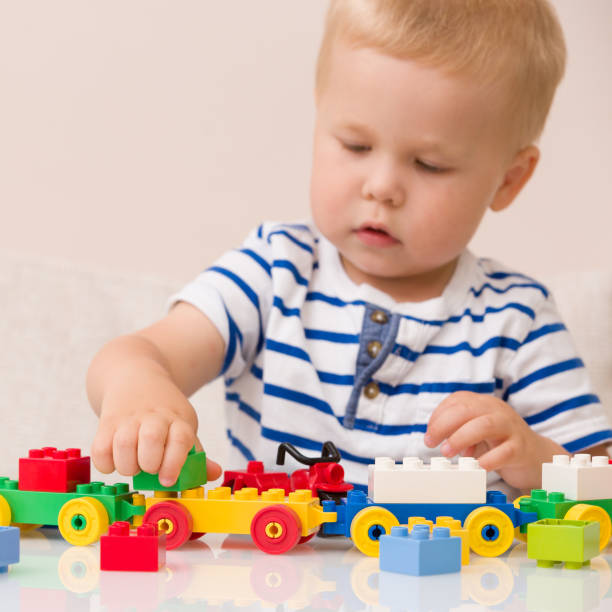 istock Toddler boy playing with colorful plastic bricks at the table. Toddler having fun and building out of bright constructor bricks. Early learning.  stripe background. Developing toys 1137284989
