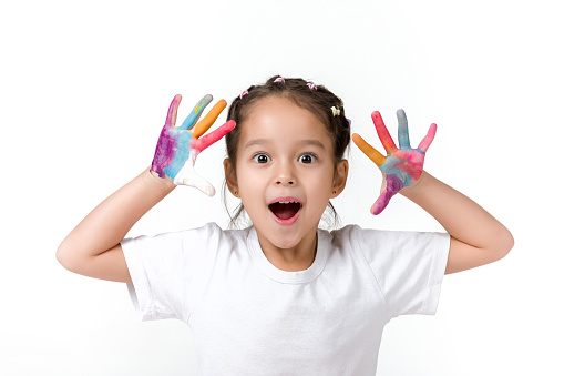 cute surprised little child girl with hands painted in colorful paint isolated on white background.