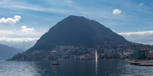 the fountain in the lake and one fishing boat, view of lake lugano and the monte san salvatore - ticino canton mountain lake lugano lake imagens e fotografias de stock