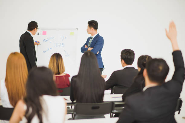 istock Young Asian people audiences seminar group raising up hand for asking the speaker that allow to raising up hand in question and answer time in meeting room see from back side of room. 1137291524