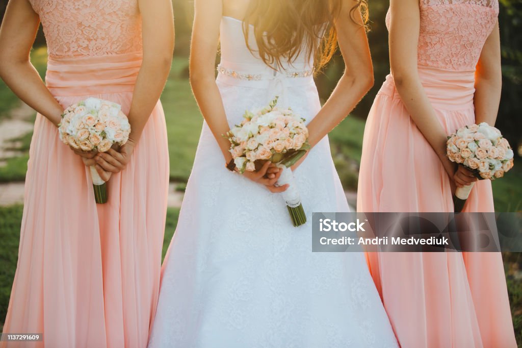 La Novia Y Las Damas De Honor En Un Elegante Vestido Está De Pie Y Sosteniendo Ramos De Manos De Flores De Color Rosa Pastel Y Verdes Con Cinta En La Naturaleza La Novia Y Las Damas De Honor En Un Elegante Vestido Está De Pie Y Sosteniendo Ramos De Manos De Flores De Color Rosa Pastel Y Verdes Con Cinta En La Naturaleza