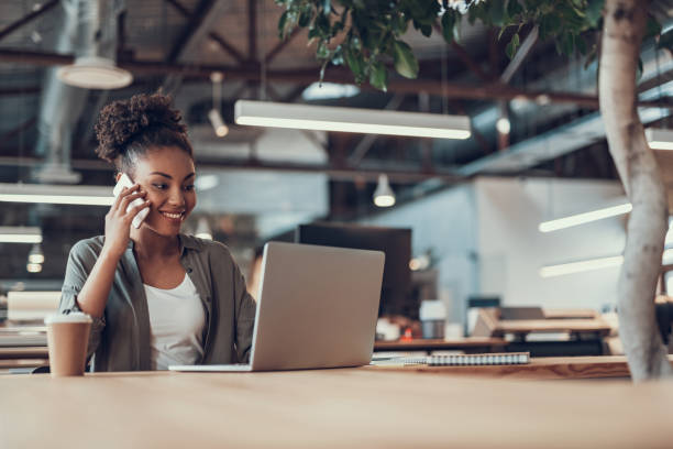 istock Beautiful afro american girl talking on cellphone while using laptop 1137297022