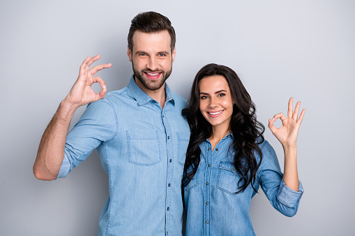 Close up portrait two amazing she her he him his couple lady guy couple stand close hold hands arms show okey symbol wear casual jeans denim shirts outfit clothes isolated light grey background.