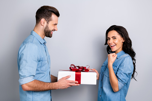 Great finally! Profile side view photo of beautiful successful wavy-hair casual student getting gift box from her stubble fellow raising fists dressed in blue denim shirts isolated argent background.