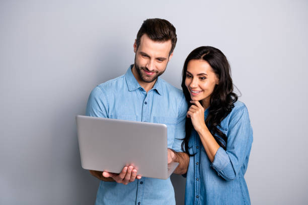 Portrait of charming inspired students using electronic devices watching videos browsing sites social networks isolated dressed in blue denim clothing on gray background