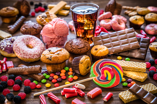 Assortment of products with high sugar level like candies, gummy candies, soda, donuts, chocolate, lollipop, wafers and cupcakes on rustic wooden table. Low key DSLR photo taken with Canon EOS 6D Mark II and Canon EF 24-105 mm f/4L