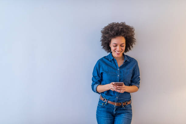 istock Smiling lovely young woman standing and using cell phone over grey background 1137313586