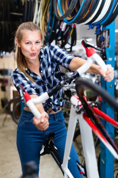 Portrait of happy  positive smiling girl who is standing with bicycle in store.