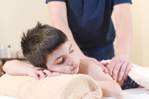 close up a little boy relaxes from a therapeutic massage. male massage therapist makes a medical massage to the back of a child - child little boys male caucasian imagens e fotografias de stock