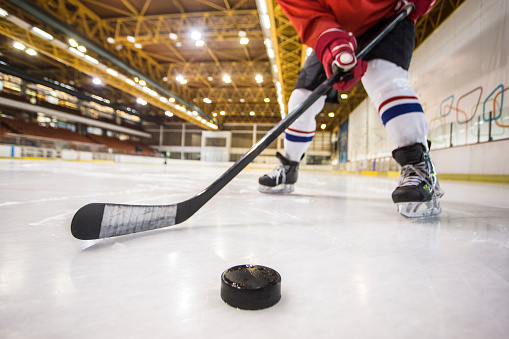 Unrecognizable ice hockey player at an ice hockey rink, holding a hockey stick.