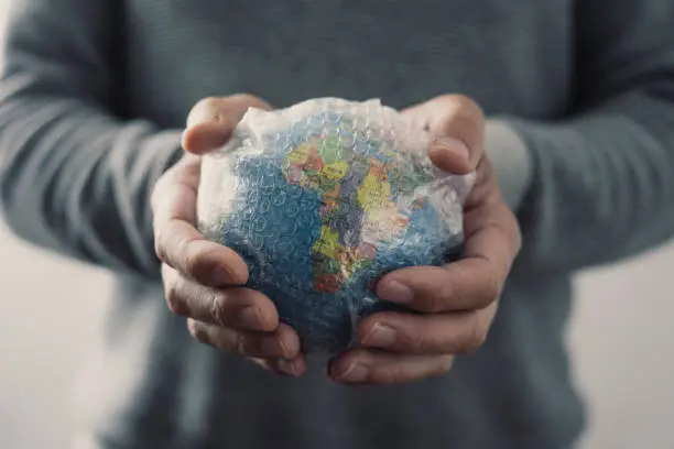 closeup of a young caucasian man with a world globe wrapped in bubble wrap in his hands