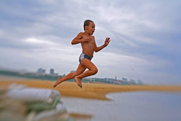 A tanned boy of six years old jumping into the water against the sky. Russia, Volga river, beach against the background of the city.