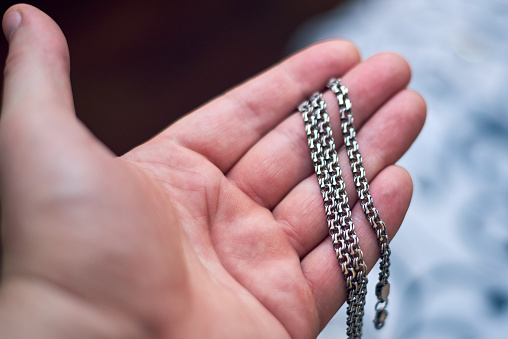 On the hand of a man lies a silver thick chain, close-up