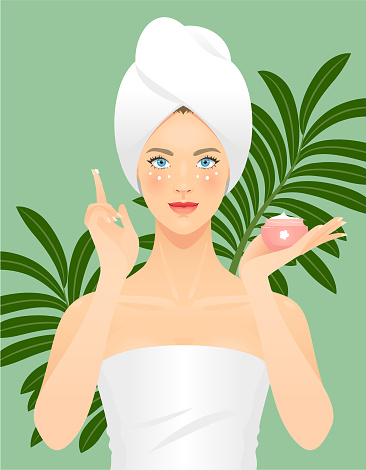 Young woman applying a face cream or a facial mask on her skin on a green background with tropical leaves.