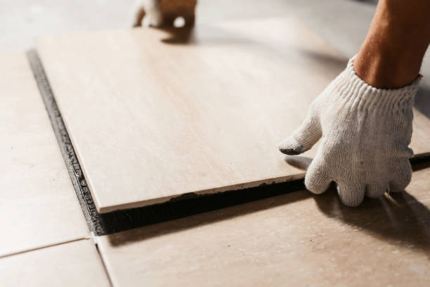 le mani del piastrellatore stanno posando la piastrella di ceramica sul pavimento. primo scatto macro. ristrutturazione della casa e costruzione di un nuovo concetto di casa - pavimento di mattonelle foto e immagini stock