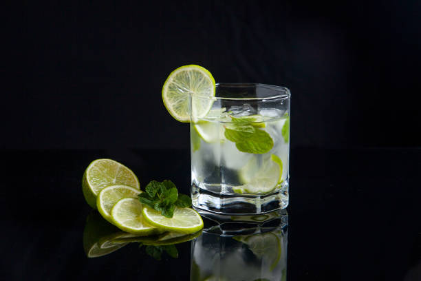 Mojito summer beach refreshing tropical cocktail in glass with soda water, lime juice, mint leaves, sugar, ice and rum on reflective black surface.